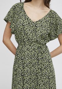 Svart blommig klänning med V-ringning, korta volangärmar och midjeband. Mönstret innehåller små vita och gröna blommor på en mörk bakgrund.