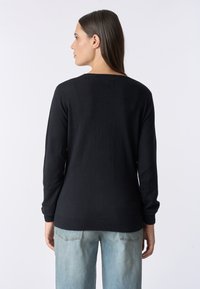 Maglione nero realizzato in morbido tessuto, con maniche lunghe e scollatura ampia. L'orlo e i polsini presentano una trama a costine. Abbinato a jeans chiari in denim.