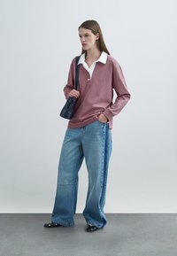 Ροζ πόλο μπλούζα με μακριά μανίκια και λευκό γιακά, σε συνδυασμό με ανοιχτό μπλε τζιν παντελόνι με φαρδιά μπάρα και έντονη ραφή στο πλάι. Μαύρη τσάντα και παπούτσια.