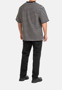 Černobílé pruhované tričko s krátkým rukávem a volným střihem, doplněné černými kalhotami a robustními černými botami.