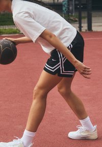 Black athletic shorts with white accents, a loose white t-shirt, and white sneakers, dribbling a basketball on a red court.
