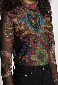 Colorful, sheer black turtleneck top featuring intricate red, blue, and green patterns, with long sleeves and a fitted design.
