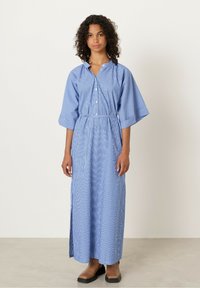 Abito lungo a righe blu con bottoni sul davanti, maniche larghe e vita svasata. Il tessuto è leggero, con una texture liscia e fessure laterali.