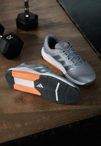 Zapatillas deportivas grises con parte superior de malla, detalles en el exterior naranja y detalles en blanco. Cuenta con una suela texturizada para mayor agarre y un diseño de cordones.