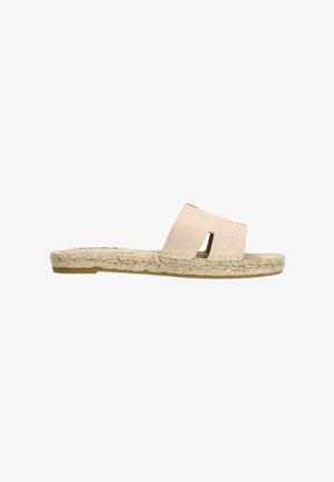 Des sandales à enfiler beige clair avec un dessus en suède, présentant un design découpé. La semelle est en jute avec une base plates pour plus de confort.