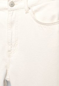 Gros plan sur l'avant d'un jean blanc en denim montrant un bouton métallique, une boucle de ceinture et le coin supérieur de la poche avec une couture visible.