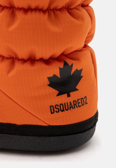 Gros plan d'une botte d'hiver matelassée orange avec une semelle noire, un logo feuille d'érable noir et le nom de la marque DSQUARED2 sur le côté.
