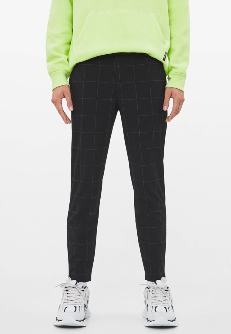 Svarta rutiga byxor med slim fit, med ett rutig mönster, tillsammans med en ljusgrön hoodie och vita sneakers.