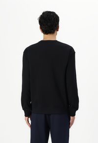 Sudadera negra hecha de una mezcla de algodón, con un cuello redondo, puños acanalados y un corte relajado. Textura suave sin adornos visibles.