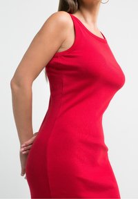 Robe sans manches rouge avec une texture côtelée, un design ajusté, un col rond et un panneau latéral qui souligne une silhouette lisse.