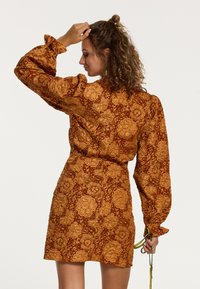 Braun gemustertes Kleid mit Blumenmotiv, mit puffärmel, tailliertem Schnitt und strukturierter Oberfläche. Akzente in Gold im Design.