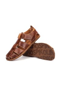 Sandale pour homme en cuir marron avec bout fermé, bride ajustable et semelle texturée comportant le nom de la marque en relief.