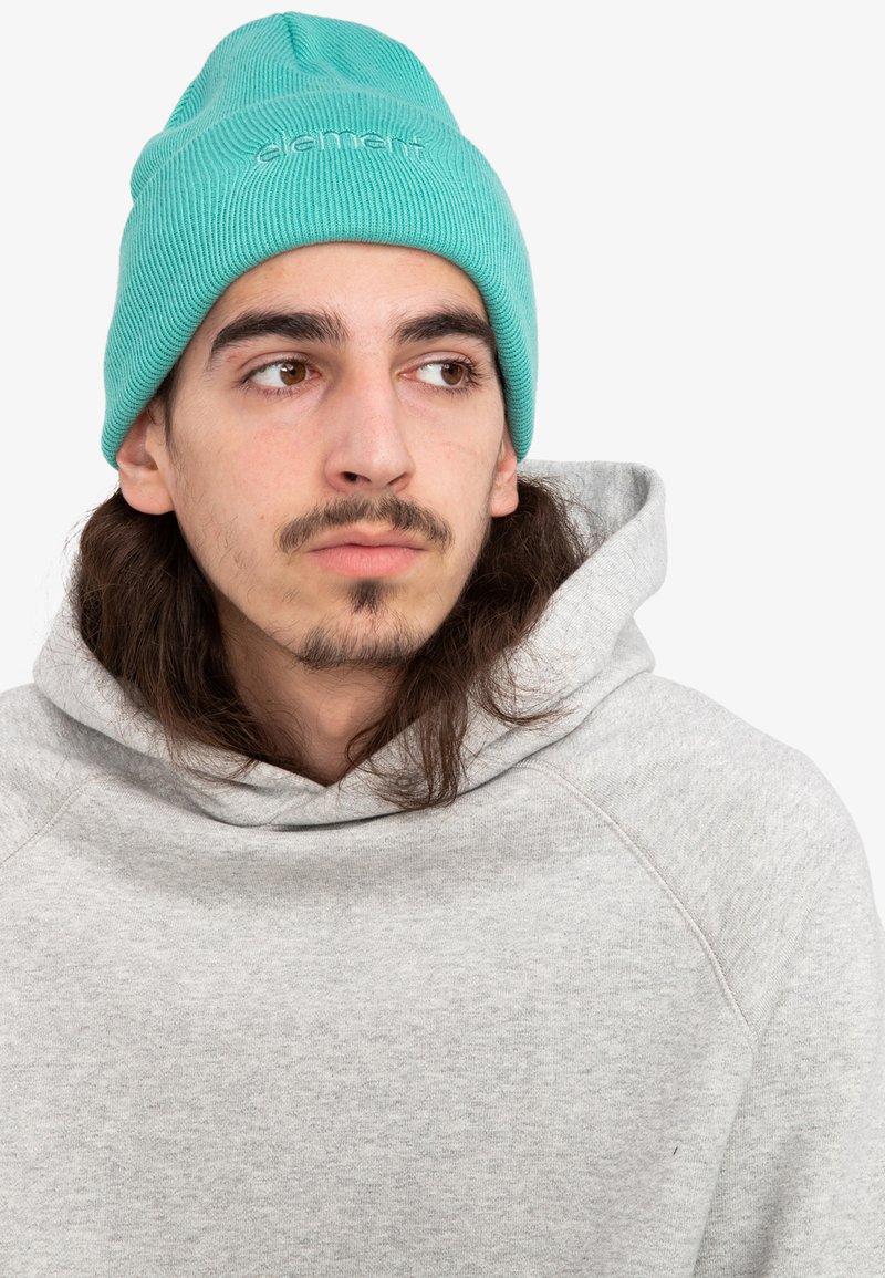 Beanie turchese con texture a coste e ricamo frontale, abbinato a una felpa con cappuccio grigio chiaro, caratterizzata da un neckline dalla vestibilità comoda.