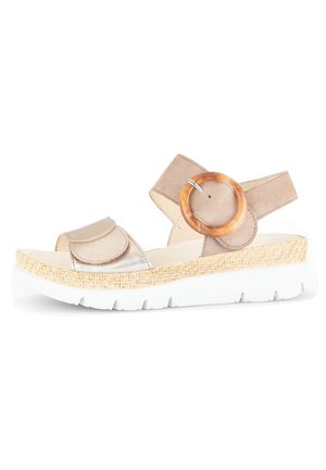 Beige sandal with textured straps, circular wooden accent, and a white rubber sole. Features a woven jute-like detailing on sole edge.