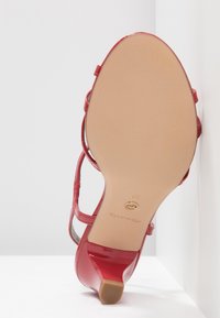 Sandale à talon haut en cuir verni rouge vue par la semelle, montrant une semelle beige lisse et un petit talon bloc.