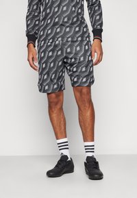 Grå atletisk trøje med geometrisk mønster; matchende shorts har et lignende design. Sorte fodtøj og hvide sokker med sorte striber fuldender looket.
