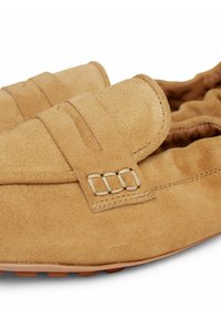 Mocassins de conduite en daim beige avec des accents cousus et une semelle souple et flexible conçue pour un usage décontracté.