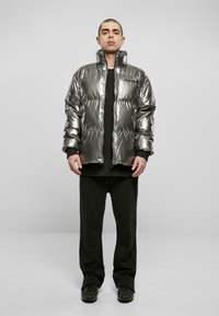 Doudoune argentée brillante avec un col haut, un design matelassé et des accents noirs. Associée à un sweat-shirt noir et un pantalon ample.
