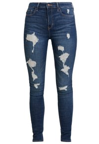 Mörkblå smala jeans i denim, med flera slitna lappar och hög midja. Påtagliga fransiga detaljer genomgående.