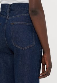 Donkerblauwe denim jeans met een hoge taille, voorzien van oranje stiksel, twee achterzakken en een rechte pijp.
