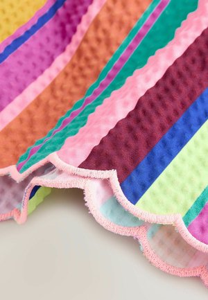 Pestrá pruhovaná látka s texturovaným povrchem, s vlnitými okraji a růžovým ozdobným lemem ve tvaru mušle. Barvy zahrnují zelenou, fialovou a oranžovou.