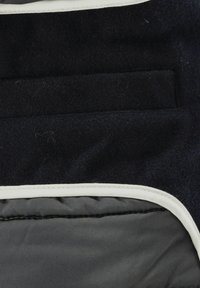 Nahaufnahme einer Tasche einer dunklen Stoffjacke über einem grauen gepolsterten Abschnitt mit weißem Nahtbesatz.