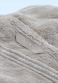Manta de forro polar en color beige claro con una superficie suave y texturizada. Presenta un borde cosido y una etiqueta beige con la marca "LUIN LIVING".