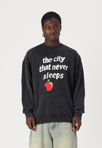 Gray oversized sweatshirt with a crew neckline. Features white text reading "the city that never sleeps" and a red apple graphic.