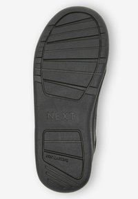 Semelle de chaussure en caoutchouc noir avec motif de relief texturé ; présente le nom de la marque "NEXT" en relief et une étiquette "NON MARQUANT" pour une meilleure adhérence.