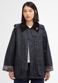 Casaco impermeável azul-marinho com colarinho de cotim, botões de pressão, dois bolsos frontais e detalhes em padrão xadrez nas mangas.