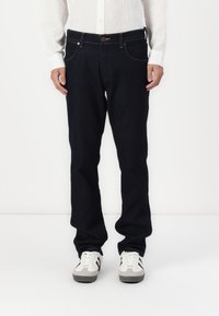 Donkerdenim jeans met een rechte pijp, vijf zakken en contrasterende stiksels. Gecombineerd met een wit overhemd met knopen en sneakers.