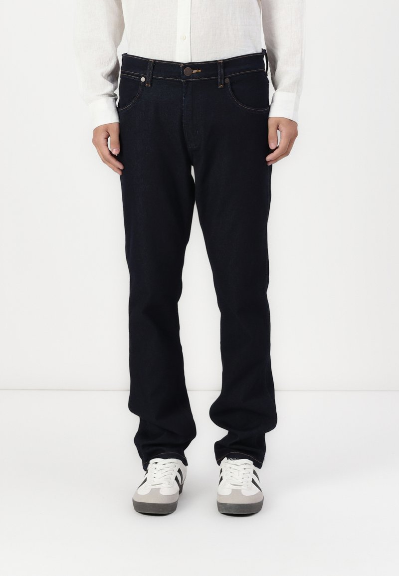 Donkerdenim jeans met een rechte pijp, vijf zakken en contrasterende stiksels. Gecombineerd met een wit overhemd met knopen en sneakers.