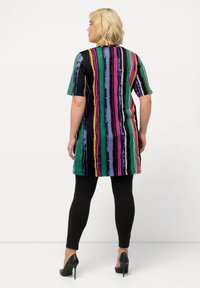 Túnica multicolor con rayas verticales en verde, púrpura, rosa y amarillo. Combinada con leggings negros y tacones altos. Mangas cortas.