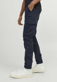 Pantalons cargo navy avec poignets élastiques et poches latérales, fabriqués en tissu résistant. Portés avec des baskets blanches et des chaussettes grises.