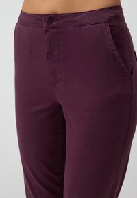 Pantalons bordeaux en coton mélangé, avec une texture lisse, une coupe ajustée, des poches avant et une fermeture à un bouton à la taille.