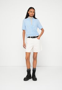 Gaiši zils īsām piedurknēm cardigans ar pogu aizdari, komplektā ar baltām šortiem un melnām šņorzābakām ar pelēkām adītām aprocēm. Minimālistisks dizains.