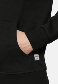 Black hoodie featuring a front pocket, ribbed cuffs, and a small label on the hem. Soft fabric with a smooth texture.