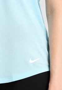 Jasnoniebieska koszulka sportowa Nike z krótkim rękawem, gładka w dotyku, z białym logo na dole; w zestawie z czarnymi legginsami.
