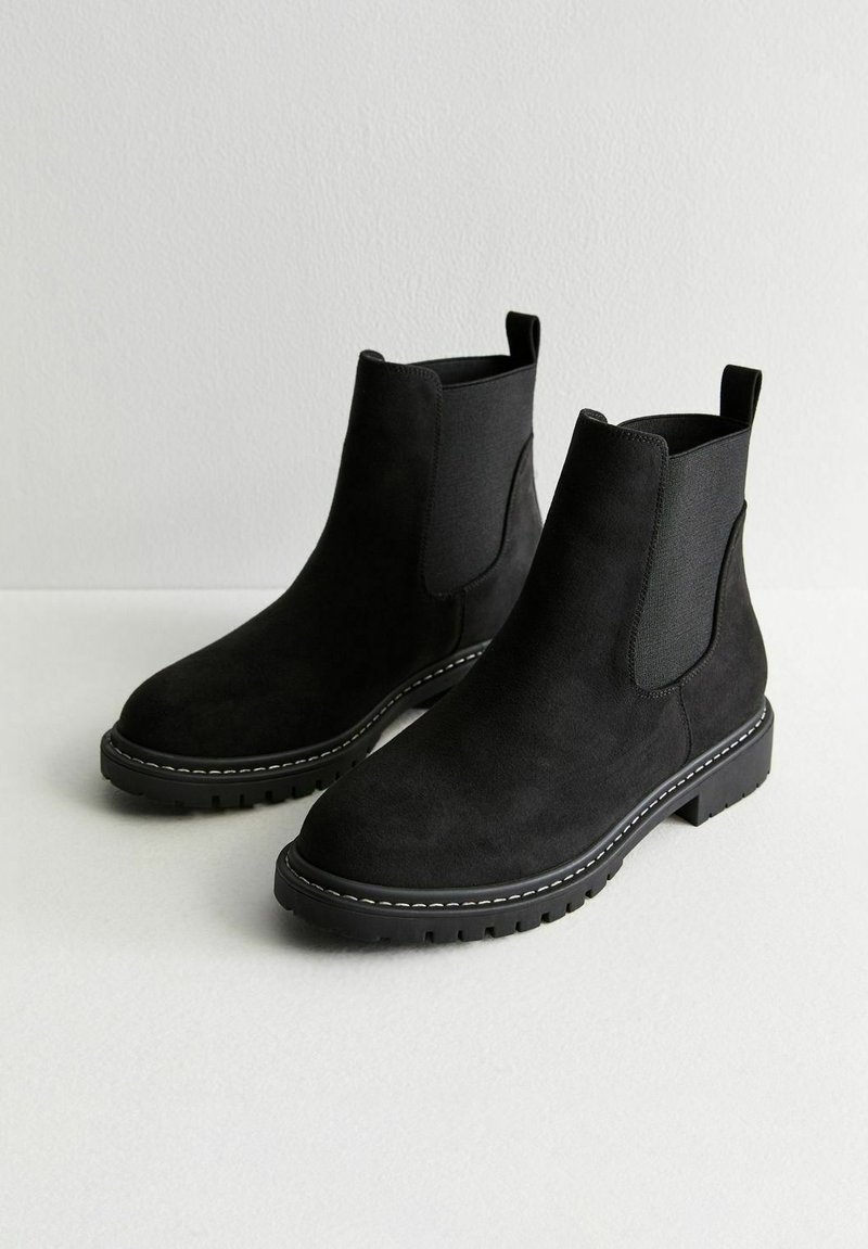 Schwarze Wildleder-Chelsea-Stiefel mit elastischen Seiteneinsätzen, strukturierter Oberfläche, leicht erhöhtem Absatz und kontrastierenden weißen Nähten entlang der Sohle.