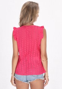 Rosa Baumwolloberteil mit Rüschärmeln, das offene Lochmustern zeigt. Der Rücken ist tailliert und passt zu hellen Denim-Shorts.