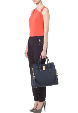 Sac navy avec accessoires en or, texture lisse, poignées doubles et forme structurée. Porté avec un haut corail et un pantalon noir.