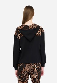 Felpa nera con accenti in stampa leopardata sulle spalle e sul cappuccio. Texture morbida, taglio rilassato e polsini a coste. Abbinata a pantaloni in stampa leopardata coordinati.
