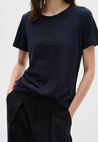 Kara zila T-kreklu ar īsām piedurknēm no mīksta, teksturēta auduma, apvienots ar melniem augsta vidukļa biksēm ar krokām priekšpusē.