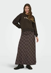 Sudadera marrón con texto beige claro, combinada con una falda larga a cuadros marrón con un detalle de botones y botas negras hasta el tobillo.