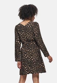 Vestido negro ajustado con mangas largas, que presenta un patrón de leopardo en beige. Textura suave, escote en V y detalle de lazo en la cintura.