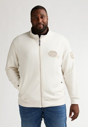 Chaqueta ligera para hombre en beige claro con cierre de cremallera, patrón texturizado, cuello alto y detalle de logo en el pecho. Incluye bolsillos laterales y puños acanalados.
