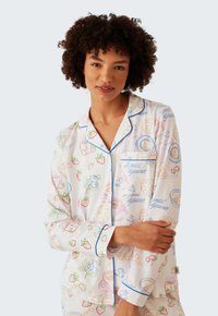 Långärmad pyjamasöverdel i mjukt vitt tyg med färgglada frukostmotiv, har blå kantning längs kragen och ärmarna.