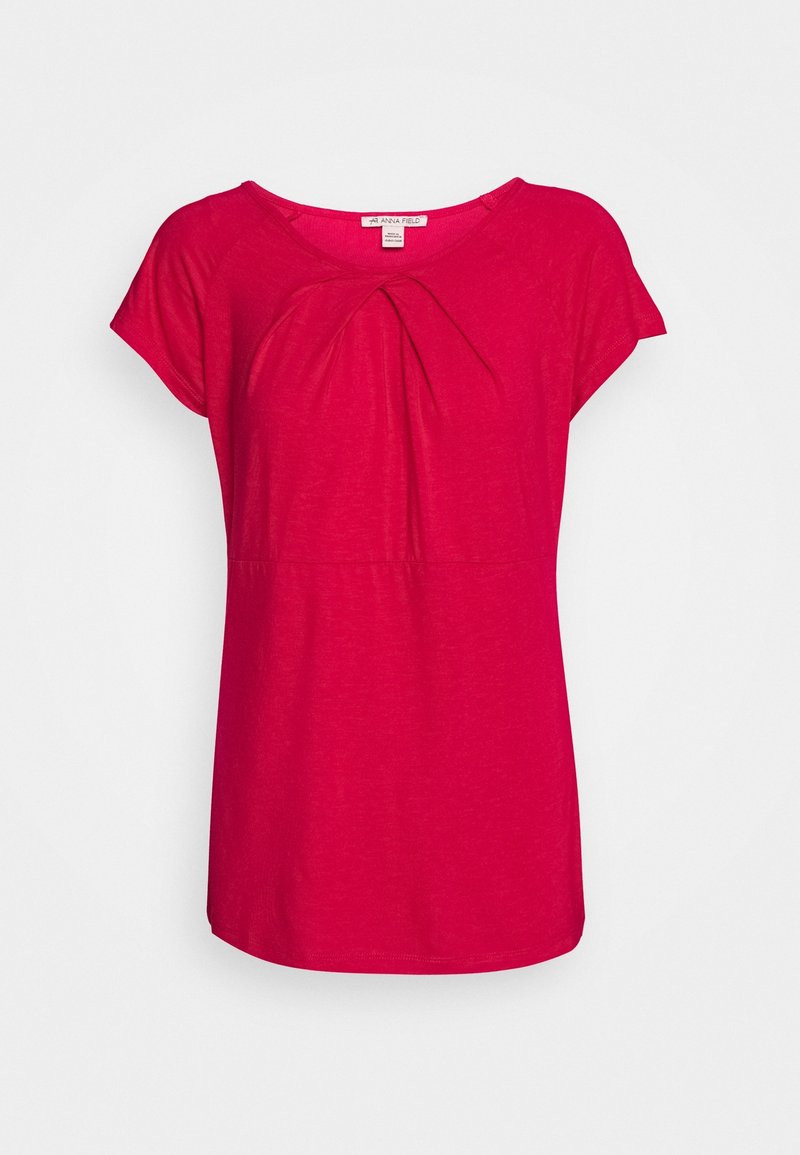 Blouse rose vif à manches courtes avec encolure ronde et pli devant, présentée sur fond blanc.