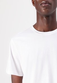 Tricou alb din bumbac cu guler rotund și mâneci scurte, textură netedă, design ajustat, fără modele sau embellishments vizibile.