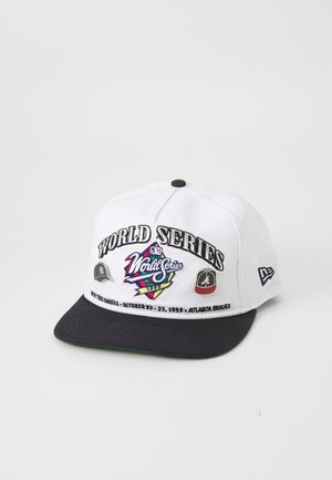 Bela bejzbol kapa z modrim obodom, izšito besedilo "SVETOVNO PRVENSTVO", logotipi ekipe in datumi dogodkov iz leta 1999. Ima plastično zaponko.